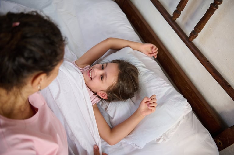A young girl smiling and laughing comfortably while her mother interacts with her warmly.